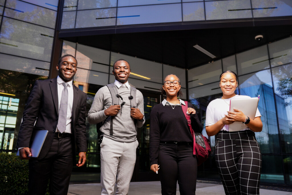 A group of 4 PVAMU students standing and smiling in front of the Business building