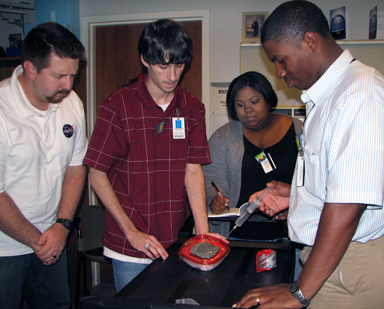 From the left, Loma Linda Proton Beam Operator Robert Meyrahn, Undergraduate Research Assistant Jordan Fuchs and Graduate Researcher Ijette Foley watch as Graduate Researcher Jullian Norman injects water into a container of "moon dirt" at the Loma Linda Medical University high energy proton beam facility in California.