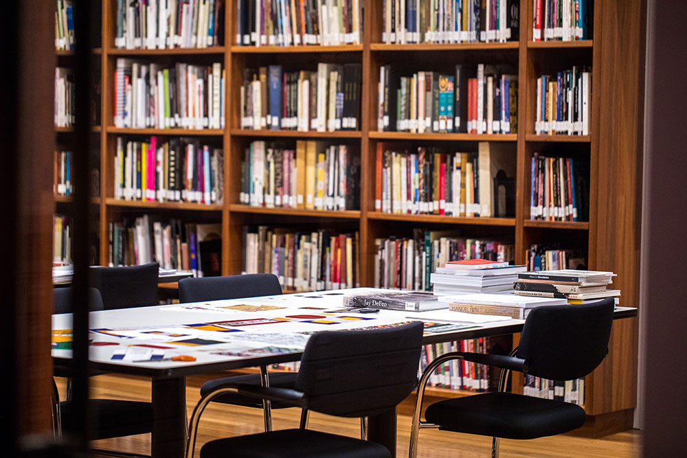 Empty chairs in a library in front of a table covered in open books