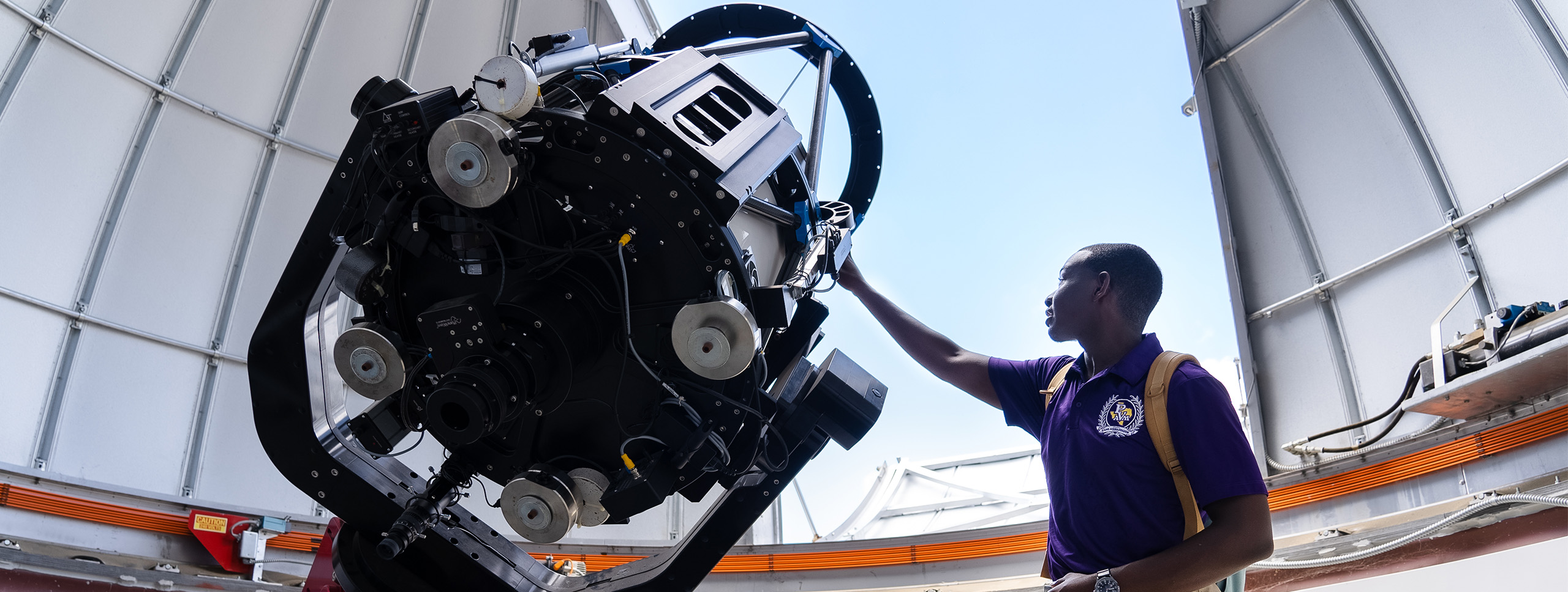 A person operates a large telescope inside an observatory, surrounded by a spacious, well-lit dome structure.