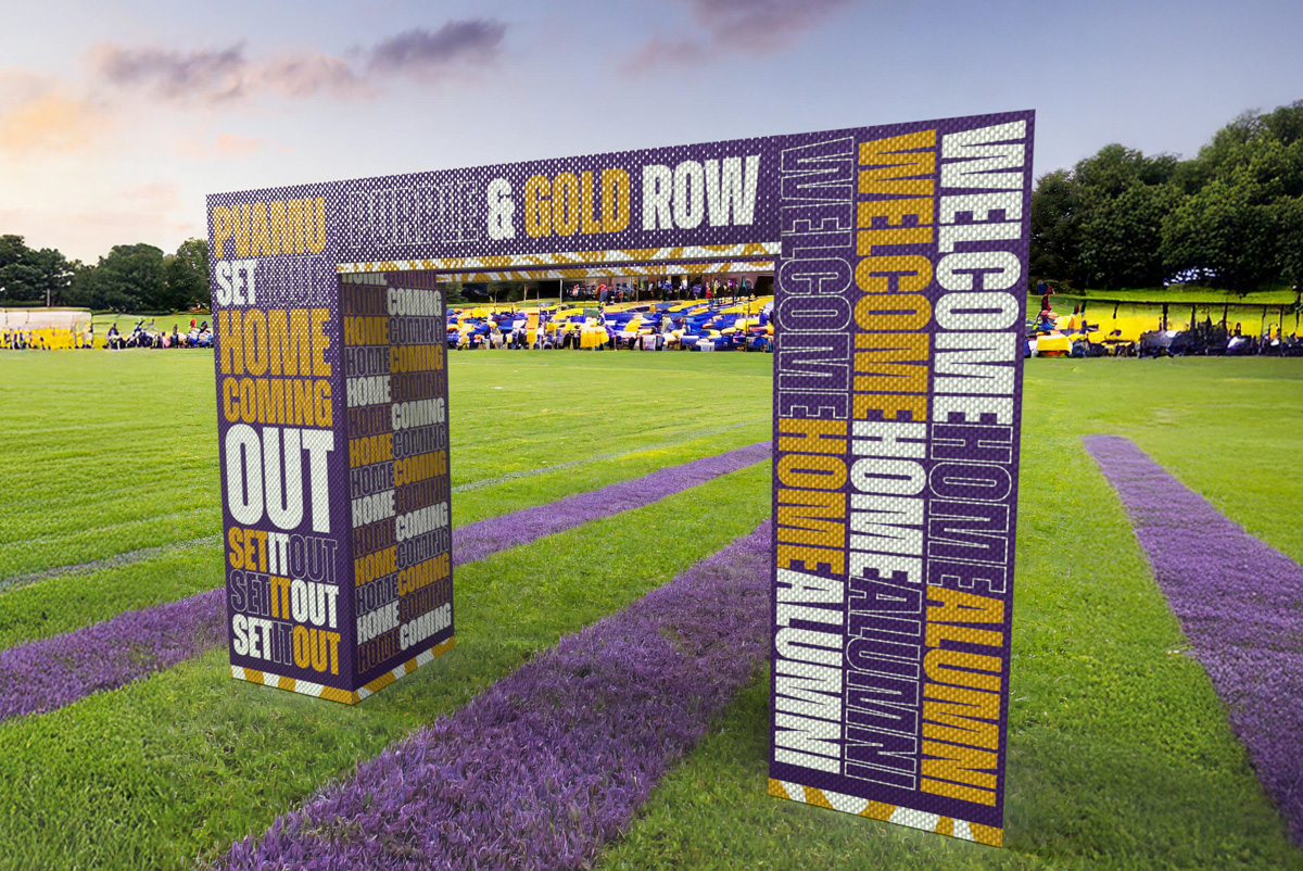 A colorful archway reading “Welcome Home Alumni” and “Homecoming” stands on a green field, with spectators in the background.