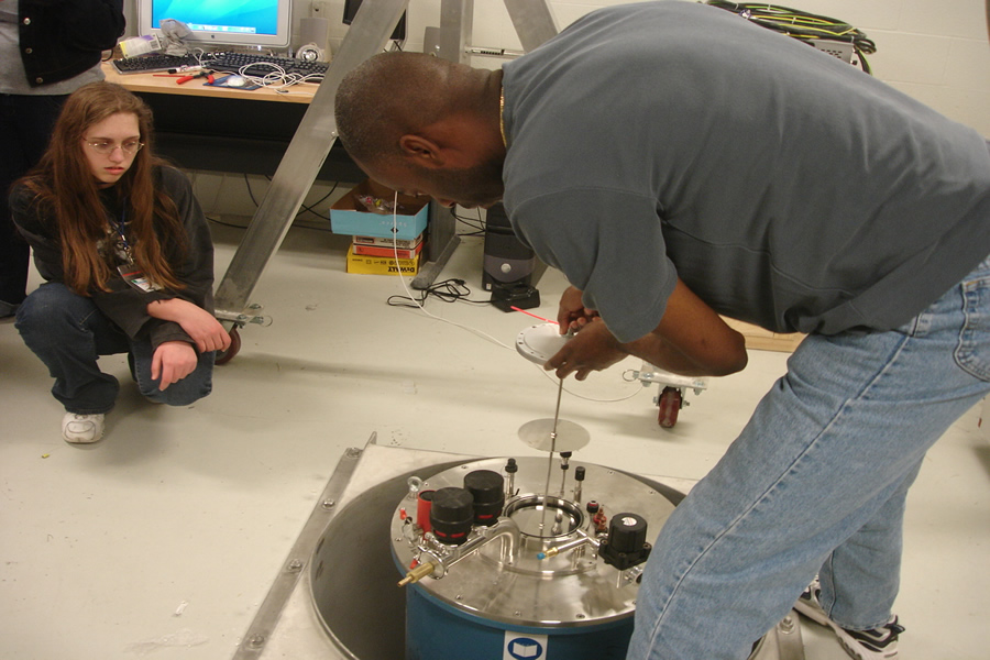 student working on equipment as another watches.